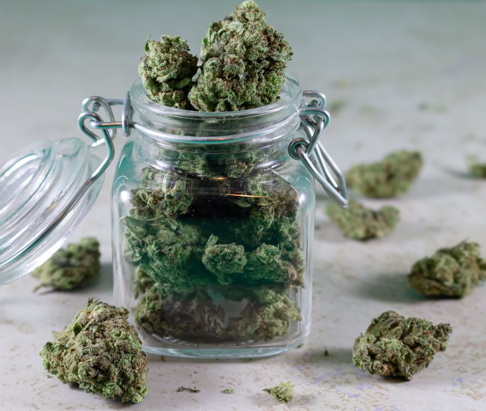 Tarro de cristal con cogollos de CBD sobre una mesa, en ambiente oscuro